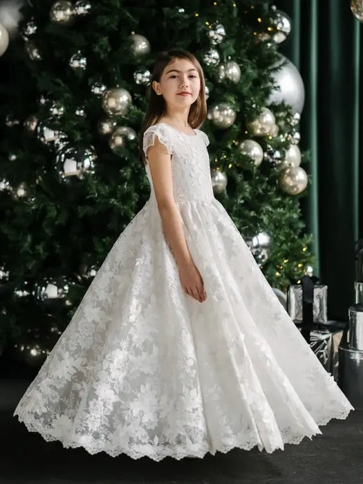 Angelica Lace Communion Dress displayed on a girl standing in front of a decorated Christmas tree.