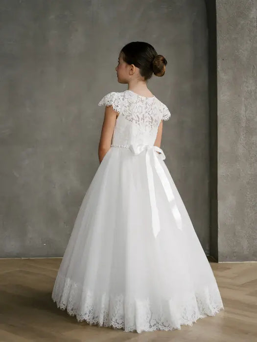 Teter Warm Ariana Lace Communion Dress shown on a girl standing indoors with a lace back and bow.
