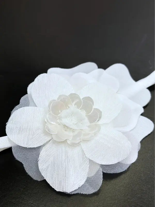 Teter Warm baby girl white headband with large layered fabric flower displayed on a dark surface.