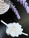 Teter Warm baby girl white flower headband displayed on a dark tabletop beside lavender flowers.