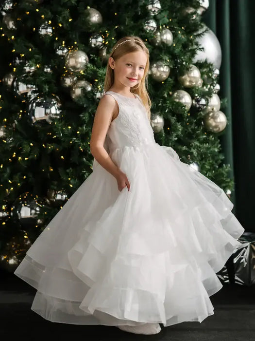 Teter Warm Billie off-white communion dress worn by a girl standing in front of a decorated Christmas tree.