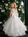 Teter Warm Billie off-white communion dress with bow, shown on a girl standing by a decorated Christmas tree.