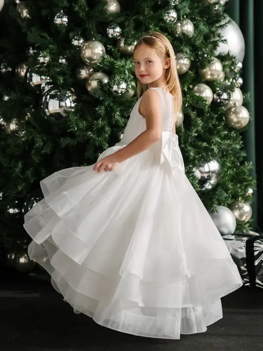 Teter Warm Billie off-white communion dress on a young girl standing in front of a decorated Christmas tree.