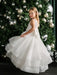 Teter Warm Billie off-white communion dress on a young girl standing in front of a decorated Christmas tree.