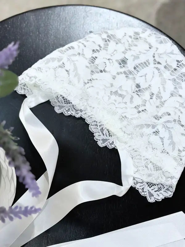 Teter Warm Bold Floral Bay Bonnet featuring white lace with ribbon ties, displayed on a table.