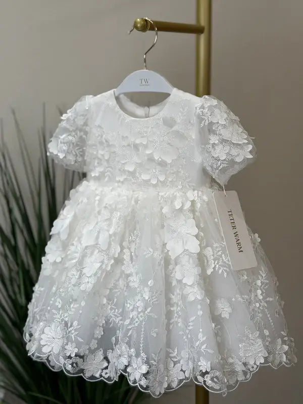 Teter Warm Carlita 3D floral lace baptism dress hanging on a white hanger against a neutral background.