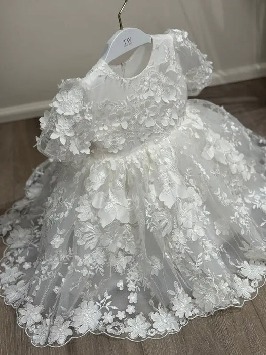 Teter Warm Carlita 3D floral lace baptism dress displayed on a hanger against a wooden floor.