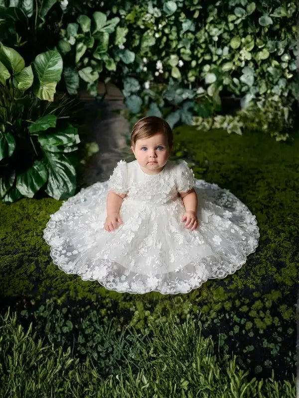 Teter Warm Carlita 3D floral lace baptism dress shown on a baby sitting on green moss.