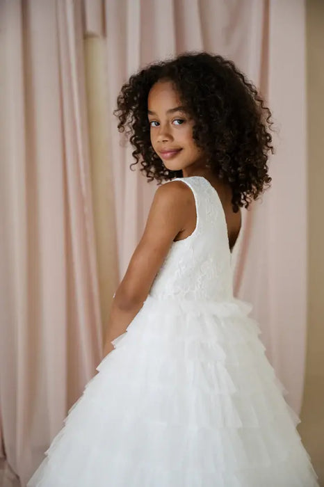 Teter Warm Celeste Off-White Communion Dress shown on a young girl standing in front of soft pink curtains.