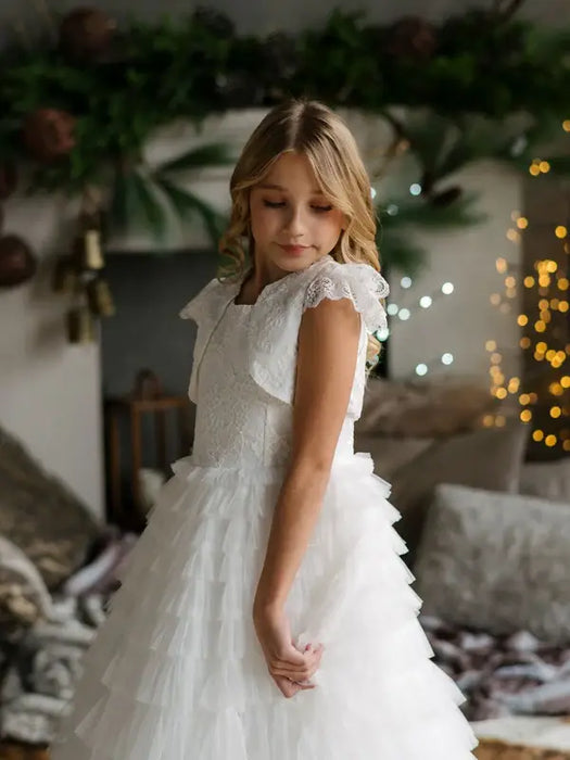 Teter Warm Celeste off white communion dress worn by a girl standing indoors near festive decor.