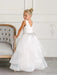 Teter Warm Cora off-white communion dress on a young girl posing beside an elegant chair indoors.
