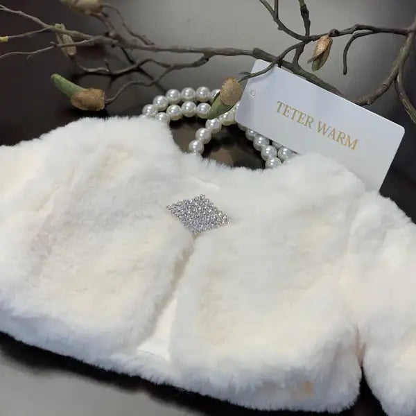 Teter Warm Dakota faux fur jacket in white displayed on a table with a pearl necklace.