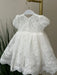 Teter Warm Dalia Floral Off-White Baptism Dress with lace details displayed on a hanger indoors.