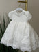 Teter Warm Dalia Floral off-white baptism dress with lace detail hanging on a hanger indoors.