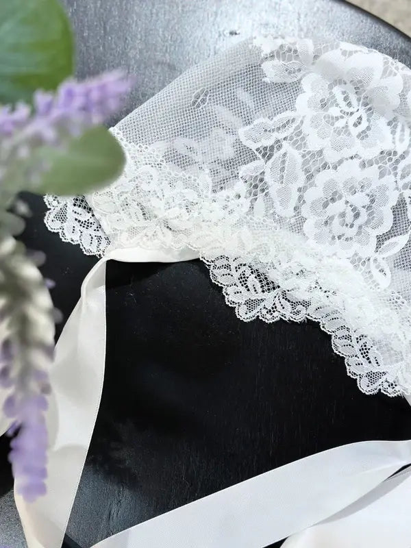 Teter Warm delicate baby bonnet with white lace and ribbon displayed on a dark surface.