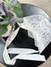 Teter Warm Delicate Baby Bonnet made of white lace with ribbon ties on a black table beside a plant.
