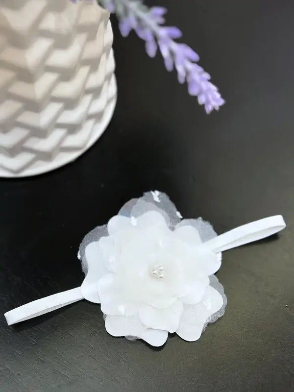 Teter Warm elegant white baby girl headband with flower detail on a dark tabletop