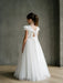 Emma Lace Communion Dress shown on a girl standing indoors, back view highlighting lace detail and bow.