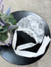 Teter Warm floral lace baby bonnet displayed on a black round table next to a vase of flowers.
