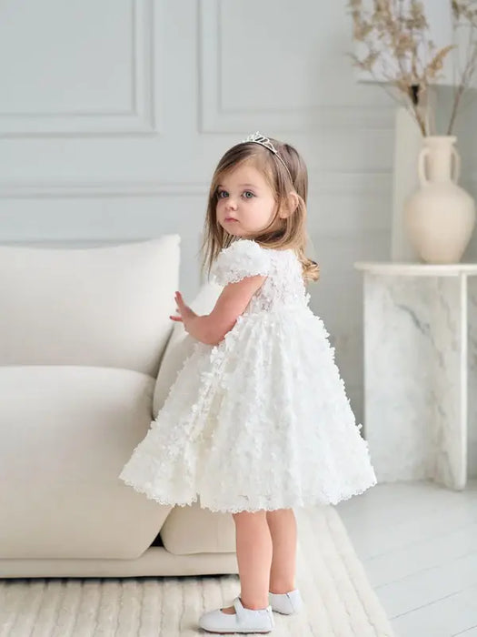 Teter Warm Floral Off-White Lace Baptism Dress worn by a young girl standing near a sofa indoors.