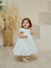 Warm floral off-white lace baptism dress on a toddler standing indoors near stairs.