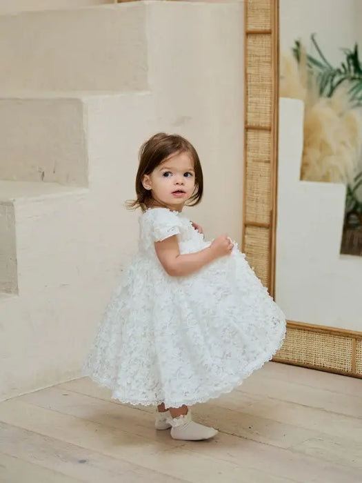 Teter Warm floral off-white lace baptism dress worn by a toddler standing indoors by a mirror.