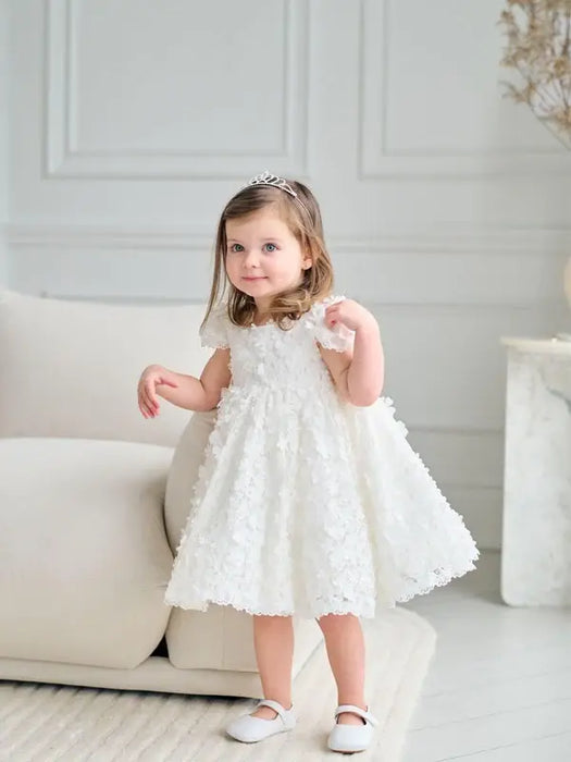 Teter Warm floral off-white lace baptism dress shown on a toddler standing in a bright living room.