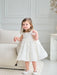 Teter Warm floral off-white lace baptism dress shown on a toddler standing in a bright living room.