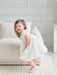 Teter Warm floral off-white lace baptism dress on a smiling toddler standing by a cream sofa.