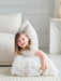 Teter Warm off-white floral lace baptism dress worn by a young girl sitting indoors on a cream rug.