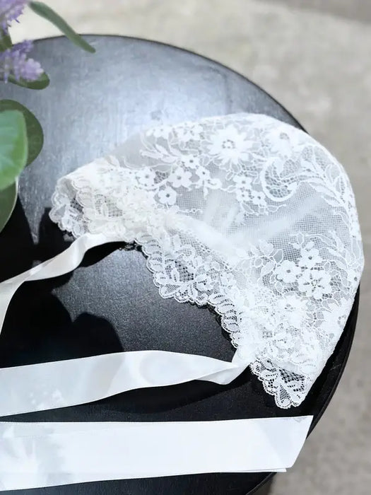 Teter Warm Floral Soft Lace Bonnet in white with floral lace detail displayed on a black tabletop.