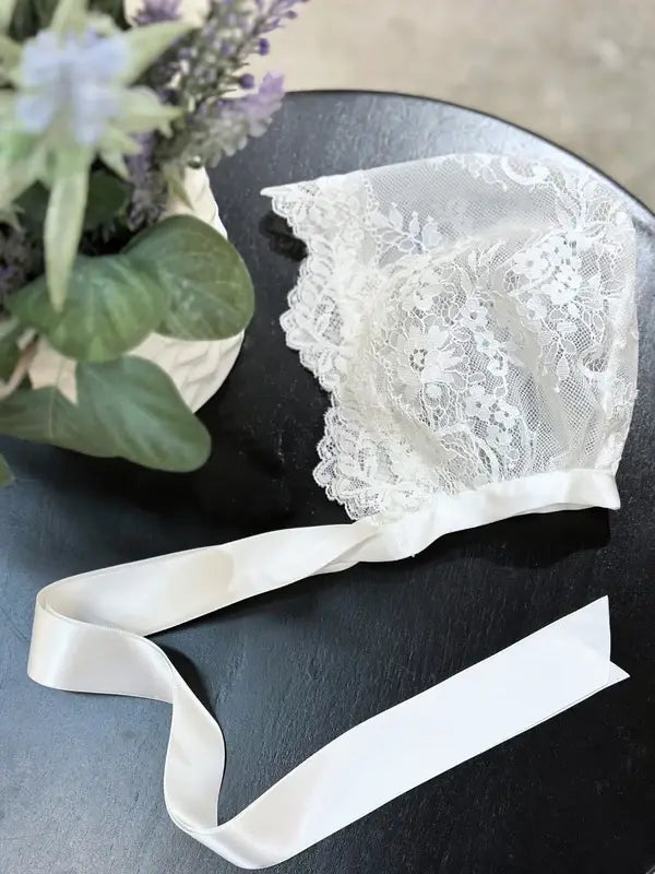Teter Warm Floral Soft Lace Bonnet displayed on a black table next to a flower arrangement.