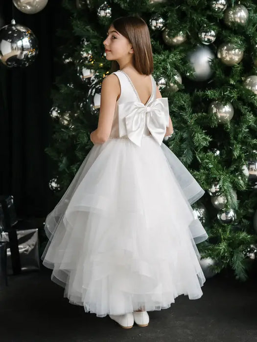 Off-white pearl communion dress with bow, shown on a girl standing by a decorated Christmas tree.