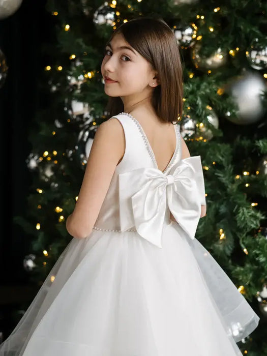 Teter Warm girl's off-white pearl communion dress with large back bow, shown by Christmas tree.