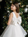 Teter Warm girl's off-white pearl communion dress with large back bow, shown by Christmas tree.