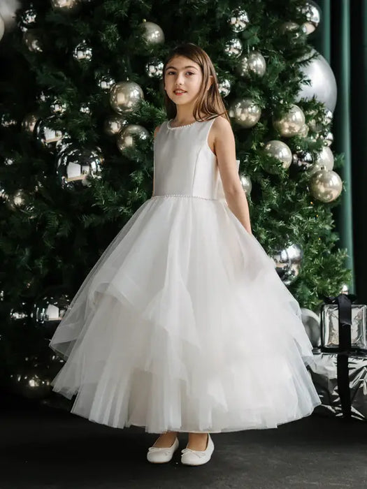 Off-white pearl communion dress for girls shown on a child standing by a decorated Christmas tree.