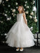 Off-white pearl communion dress for girls shown on a child standing by a decorated Christmas tree.