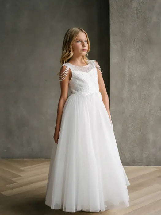 Hailey Lace Sequin Communion Dress shown on a young girl standing indoors against a grey wall.