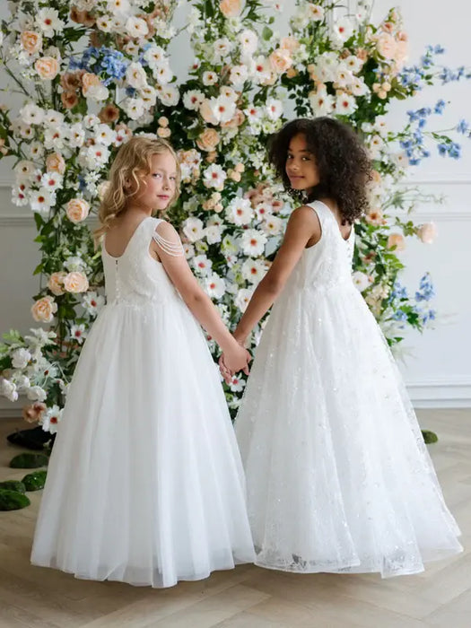 Teter Warm Hailey Lace Sequin Communion Dress shown on two girls holding hands in front of floral backdrop.