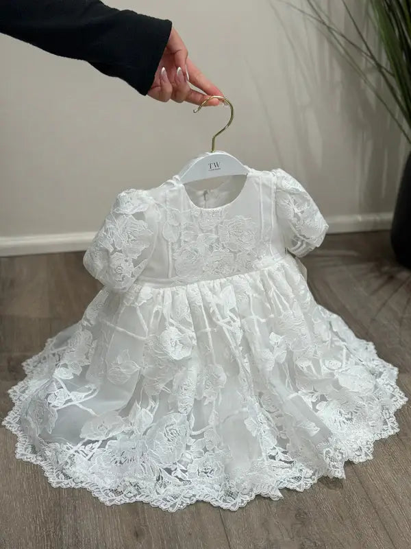 Teter Warm Hariet floral baptism dress with lace details displayed on a hanger indoors.