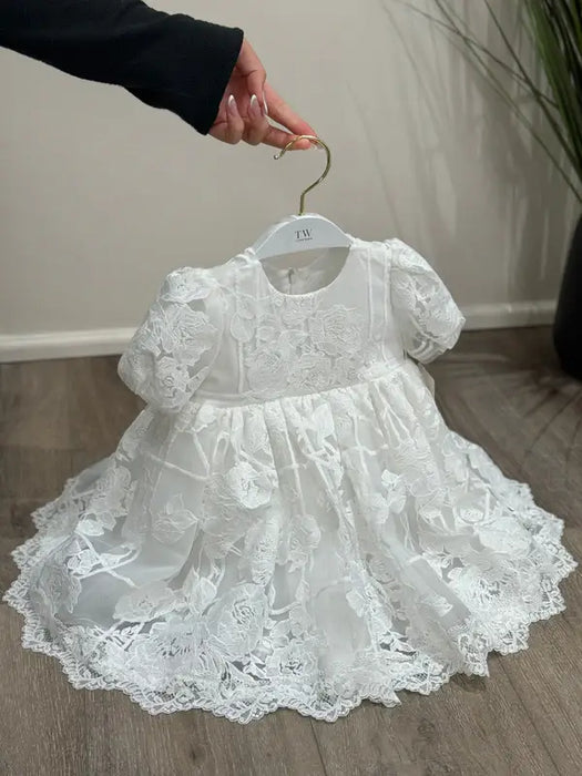 Teter Warm Hariet floral baptism dress with lace details displayed on a hanger indoors.