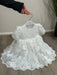 Teter Warm Hariet floral baptism dress with lace details displayed on a hanger indoors.