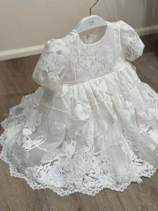 Hariet Floral Baptism Dress with lace details and three-quarter sleeves on a hanger over wood floor.