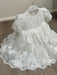 Hariet Floral Baptism Dress with lace details and three-quarter sleeves on a hanger over wood floor.