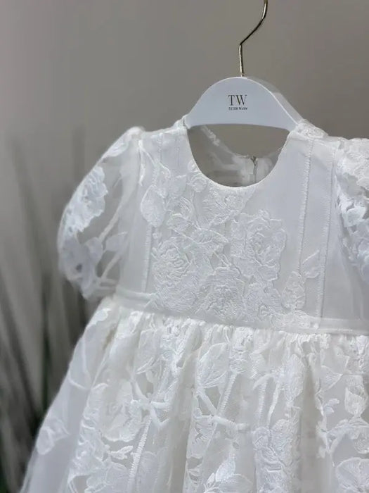 Teter Warm Hariet floral baptism dress with lace detail displayed on a hanger against a neutral background.