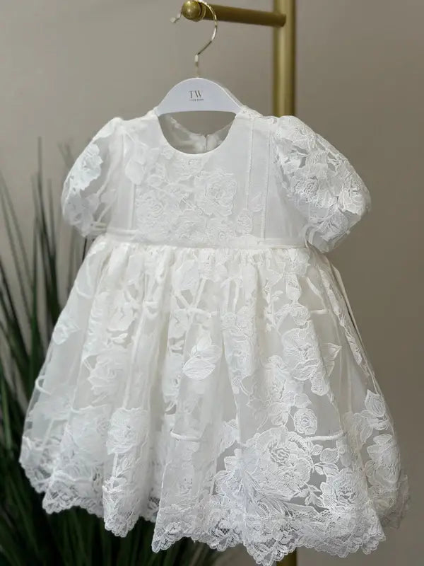 Teter Warm Hariet floral baptism dress with three-quarter sleeves, displayed on a hanger indoors.
