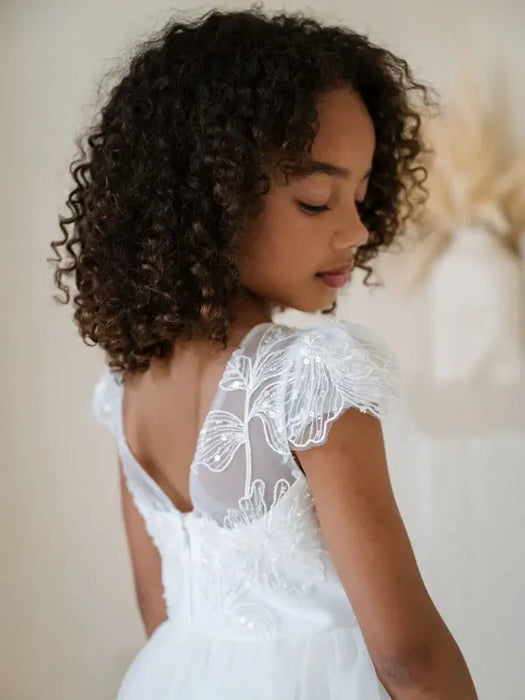 Heidi Sequin Bodice Communion Dress with floral embroidered sleeves worn by a young girl indoors.