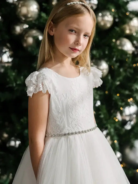 Julia off-white lace communion dress worn by a girl standing in front of a decorated Christmas tree.