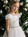 Julia off-white lace communion dress worn by a girl standing in front of a decorated Christmas tree.