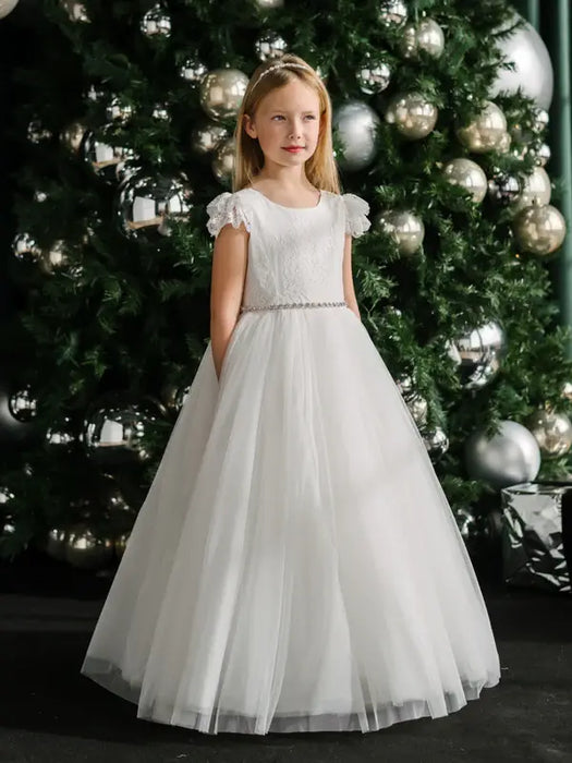 Teter Warm Julia off white lace communion dress worn by a girl standing in front of a decorated Christmas tree.